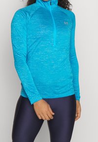 Světle modrý sportovní top s vysokým límcem, polovičním zipem a dlouhými rukávy, vyrobený z texturované, vlhkost odvádějící látky.