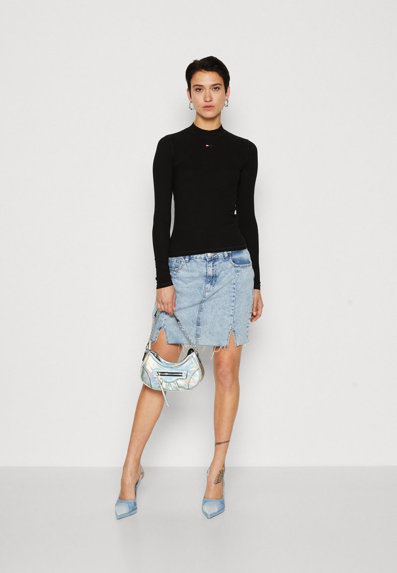 Schwarzes langärmliges Oberteil, hellblauer Jeansrock mit fransigen Kanten, schillernde Handtasche und hellblaue spitze Absätze.