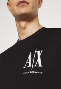 Camiseta de algodón negra con un logotipo bordado en blanco "A/X" y "ARMANI EXCHANGE" en el pecho, cuello redondo y mangas cortas.