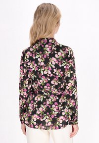 Langærmet bluse i sort stof med et levende blomsterprint i pink og grøn. Bagsiden har en krave og en skræddersyet pasform.