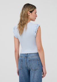 Top ribbed bluino chiaro con maniche corte a volant, design aderente, abbinato a jeans in denim sbiaditi a vita alta, visto da dietro.