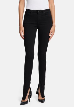 Jean skinny noir taille haute, avec des accents de zip à la cheville. Le tissu paraît lisse avec un léger éclat.