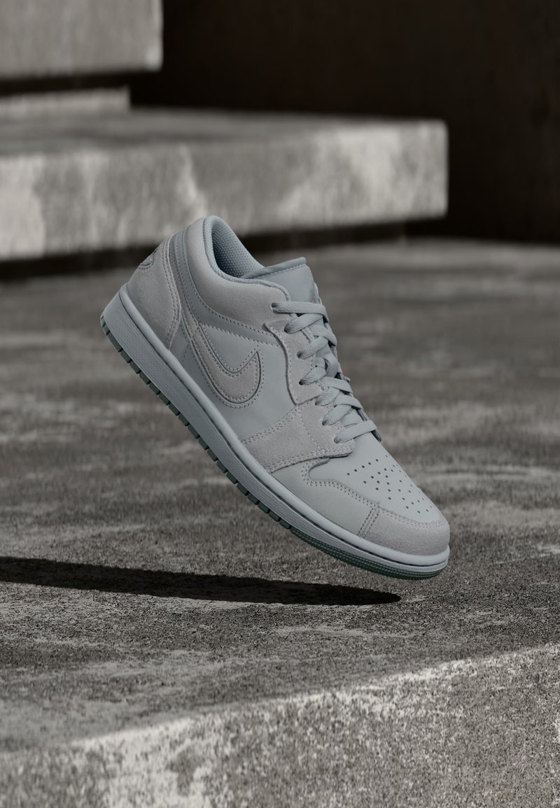 Ανοιχτόγκρι αθλητικό παπούτσι Nike να αιωρείται πάνω από τραχιές σκάλες από σκυρόδεμα με σκιές που αναδεικνύουν τα περιγράμματα και την υφή του.