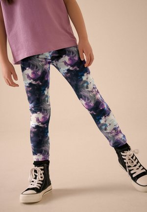 Multifarvede leggings med et svindende abstrakt mønster i nuancer af lilla, blå og sort stof. Kombineret med sorte højhælede sneakers.
