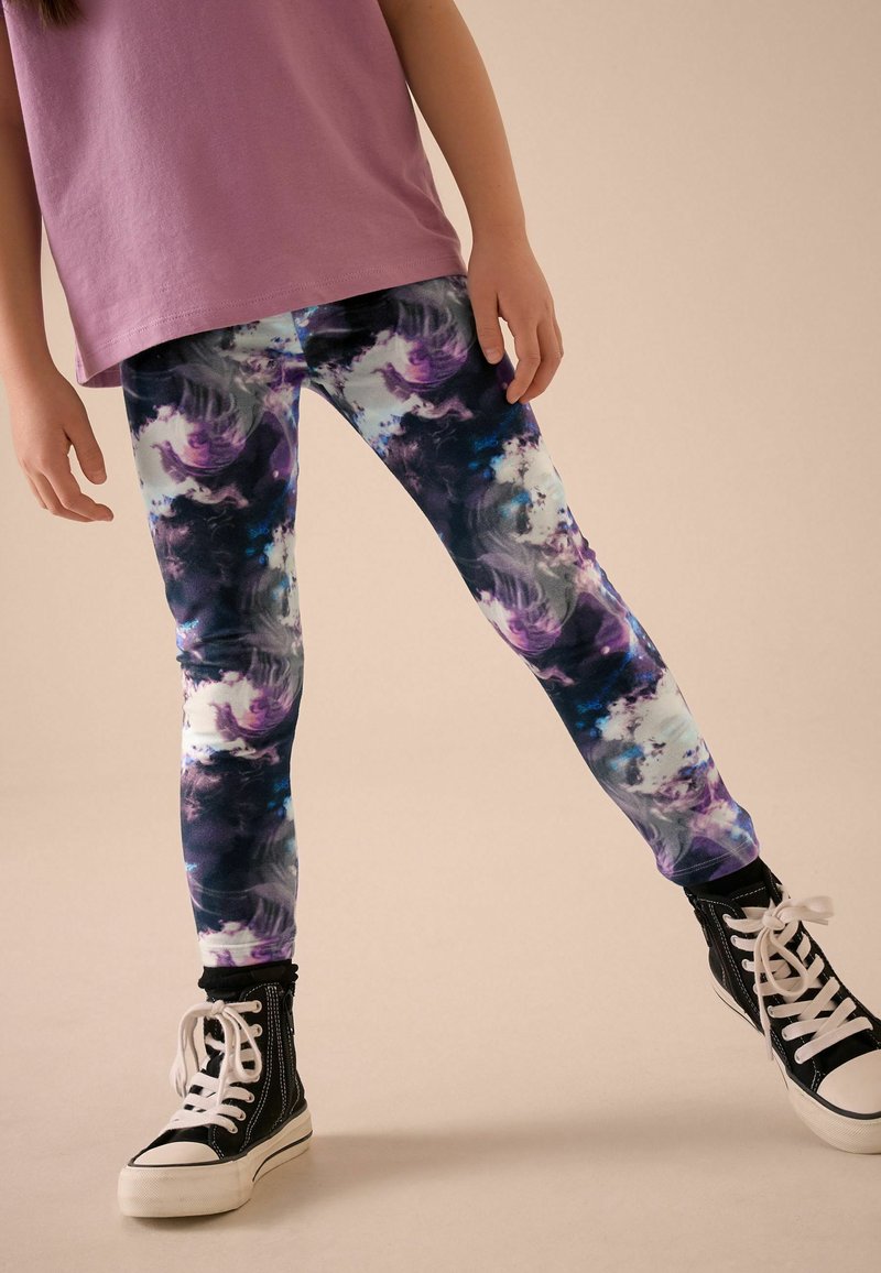 Leggings multicolores présentant un motif abstrait tourbillonnant avec des nuances de violet, bleu et tissu noir. Associés à des basket montantes noires.