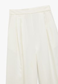 Crème-kleurige broek met plooien bij de tailleband, gemaakt van een gladde stof en met een rechte pasvorm.