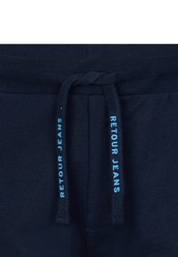 Granatowe spodnie dresowe z wkładką w pasie; sznurki są ciemne z napisem "RETENOUR JEANS" w jasnoniebieskim kolorze. Prosta, teksturowana tkanina.