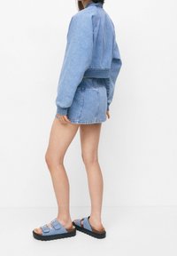 Denim jas en rok set in lichtblauw, met een cropped ontwerp, elastische tailleband, en gecombineerd met blauwe sandalen met dubbele gespen.