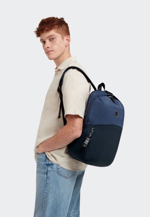 Zaino in nylon blu navy e blu scuro con spallacci regolabili, forma arrotondata, tasca frontale con zip e una toppa con logo sul davanti.