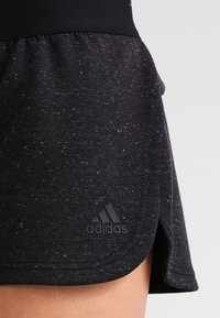 Musta urheiluhame, jossa on pistekuvioitu pinta, leveä vyötärönauha ja Adidas-logo vasemmassa alakulmassa. Kaareva helma liikkumiseen.