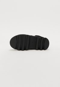 Black shoe sole with a textured, ribbed design. Features a rounded toe and contoured edges for enhanced grip and comfort.