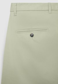 Hellgrüne Hose mit glatter Textur, ausgestattet mit einer Gesäßtasche mit schwarzem Knopfverschluss und Gürtelschlaufen.