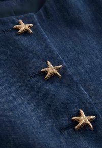 Bottoni a forma di stella marina dorata fissati su tessuto di denim blu scuro, evidenziando la texture e l'ordine su un indumento.