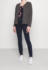 Cárdigan gris texturizado con escote en V, combinado con una blusa de estampado floral, jeans oscuros y zapatillas blancas.