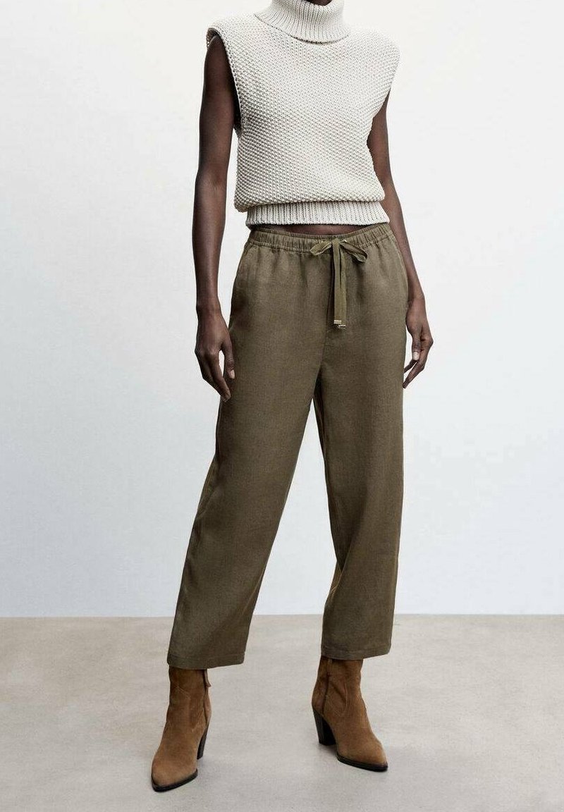 Col roulé sans manches en maille crème avec motif texturé, associé à un pantalon ample olive et des bottines à talons couleur sable.