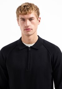 Zwarte zip-up trui met een kraag, met een gladde textuur en getailleerde pasvorm. Ribbelstructuur op de schouders, minimalistisch ontwerp, geen patronen.