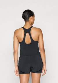 Černý sportovní top bez rukávů s designem na zádech ve stylu racerback a výřezem ve tvaru klíče, spárovaný s černými šortkami. Hladká látka, těsně padnoucí silueta.
