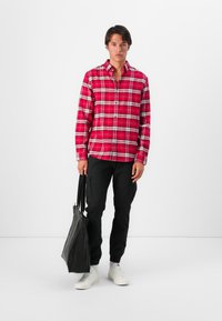 Camisa de cuadros rojos abotonada, pantalones cargo negros, zapatillas blancas y una bolsa tote negra. Tejido suave con un ajuste estructurado y patrones contrastantes.