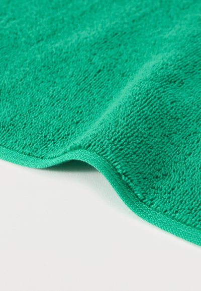 Κοντινό πλάνο ενός πράσινου μικροΐνα υφάσματος που δείχνει την υφή της επιφάνειας και τις ραμμένες άκρες σε λευκό φόντο.