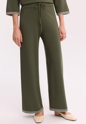 Szerokie spodnie w oliwkowym kolorze z troczkiem w talii, połączone z beżowymi spiczastymi balerinami i pasującą oliwkową bluzką z paskami na mankietach.