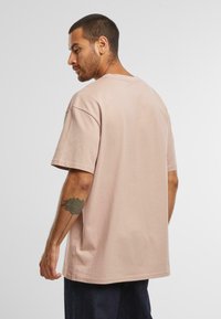 T-shirt de bumbac supradimensionat de culoare roz deschis, cu mâneci scurte și un decolteu rotund, având o textură fină și o croială lejeră.