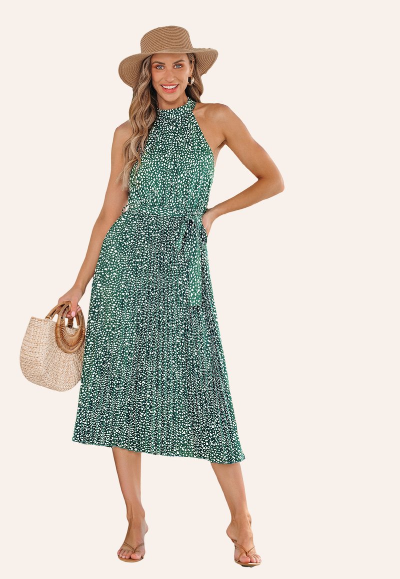 Abito verde a pois con scollatura a halter, vita cintrata e gonna fluente. Abbinato a una borsa di paglia e sandali.