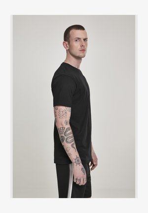 Lühikeste juustega mees, kes kannab musta särki ja lühikesi pükse, näitab oma tätoveeritud paremat kätt, millel on erinevad motiivid, sealhulgas madu ja laeva rool.