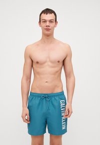 Turkio spalvos maudymosi šortai su elastine juosta ir raišteliu. Šone yra baltas "CALVIN KLEIN" logotipas. Glotni, lengva medžiaga.