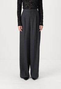 Wide-legged trousers in dark gray fabric, featuring a high waist, subtle texture, and tailored pleats. Worn with a black lace top.