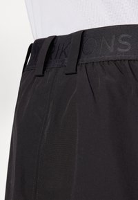 Pantalones cortos negros con textura sedosa, que cuentan con una cintura elástica con marca en relieve y un diseño de corte recto.
