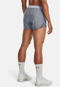 Grå sportshorts med lätt material, elastisk midjeband och sidorevor, kombinerade med vita sportstrumpor och skor.