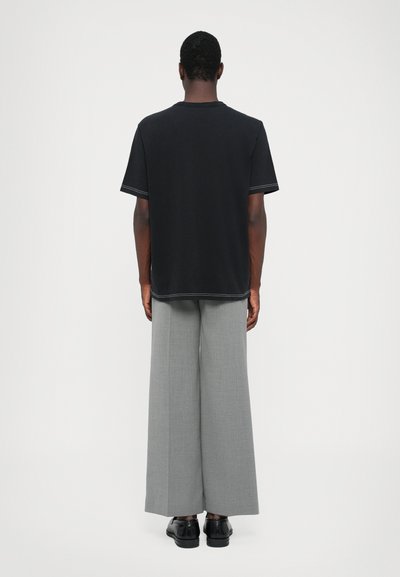 Tricou din bumbac negru, cu mâneci scurte, asortat cu pantaloni gri amplii. Tricoul are cusături contrastante pe margini.