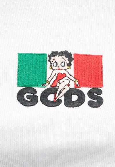 Κινούμενη γυναίκα με κόκκινο φόρεμα κάθεται ανάμεσα σε πράσινα και κόκκινα ορθογώνια μπλοκ με μαύρο κείμενο "GCDS" από κάτω σε λευκό ύφασμα.