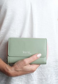 Grön och rosa plånbok av slät läder, med lockstängning, stickade kanter och präglad "VARGU 07"-logotyp. Kompakt design.
