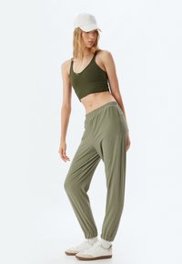Oliwkowy crop top i pasujące dresowe spodnie z elastycznymi mankietami; białe sneakersy z beżowymi akcentami. Gładki materiał z luźnym krojem.