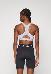 Hvit sports-bh med utskjæringsdesign og logo på kanten, kombinert med svarte høytgående shorts med merket på midjen. Slank tekstur.