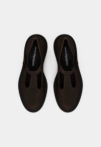 Chaussures en cuir marron avec un design en T, bout rond, semelle en caoutchouc noire et deux découpes sur le dessus. Texture douce, minimalisme dans les détails.