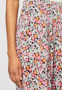 Pantalons plissés floraux avec une base noire, ornés de fleurs roses, vertes et orange. Taille élastique et texture de tissu légère.