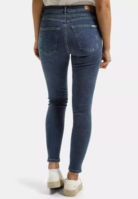 Granatowe dżinsy skinny z wysokim stanem, z dwiema tylnymi kieszeniami i skórzaną naszywką na pasku. Noszone z białymi butami.