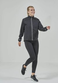 Svart vindjacka med vit dragkedja och detaljer, i kombination med svarta tights och svarta träningsskor, med en figurnära passform.