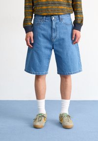 Blue denim shorts with a straight cut, featuring a classic five-pocket design and a faded texture. Worn with a striped top and sneakers.