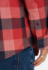 Rood en marineblauw geruit flanellen shirt met een gestructureerde weving, voorzien van knopenmanchetten en een gebogen zoom, gedragen over blauwe spijkerbroek.