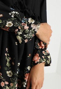 Svart klänning med blommönster i rosa, vitt och grönt; har volangärmar och mjuk, texturerad ty. 