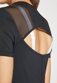 Black athletic top with sheer mesh back panel and a cut-out design. Features a round neckline and short sleeves with stitching details.