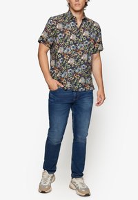 Kurzarmhemd mit dunklem Hintergrund und floralen Mustern in Blau, Orange und Grün. Getragen mit blauen Jeans und grauen Turnschuhen.