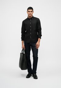 Čierna košeľa s gombíkmi, tmavo modré džínsy, čierne topánky a čierna taška. Jednoduchý dizajn, jednofarebné farby a prispôsobený strih.