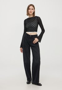 Crop top in pizzo nero con maniche lunghe, abbinato a jeans neri a gamba dritta a vita alta e ballerine nere. Design semplice e testurizzato.