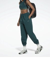 Atletisk outfit med en teal croppad topp och matchande avsmalnande joggingbyxor med elastiska muddar; kombinerat med gråa och svarta skor samt vita strumpor.