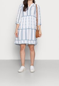 Jasnoniebieska sukienka w białe paski o tiered design, z kwiatowym haftem i zapięciem na guziki. W zestawieniu z białymi trampkami.