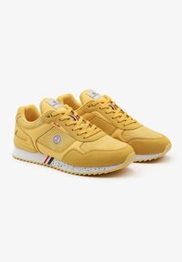Zapatillas amarillas con una mezcla de material de gamuza y malla. Presentan una suela moteada blanca y un logo en el lateral. Los cordones coinciden con el color de la parte superior.